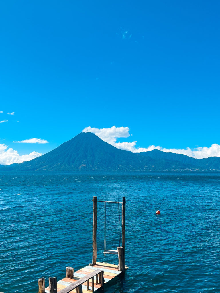 photo of a pier with a swing on the end, showing a volcano on the background of lake atitlan