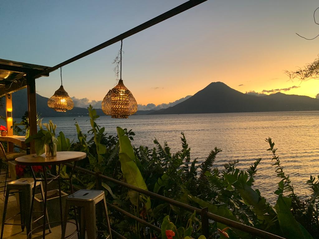 photo of the dining area at atilan sunset lodge just after sunset time. the volano and lake in the background with an orange sky. plants and lanterns in the foreground