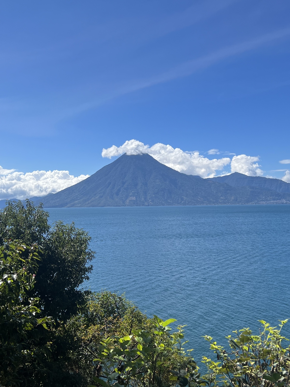 photo of lake atitlan from our room at sunset lodge. shows plants and trees in bottom corner and volcano in background with stunning blue water between the two