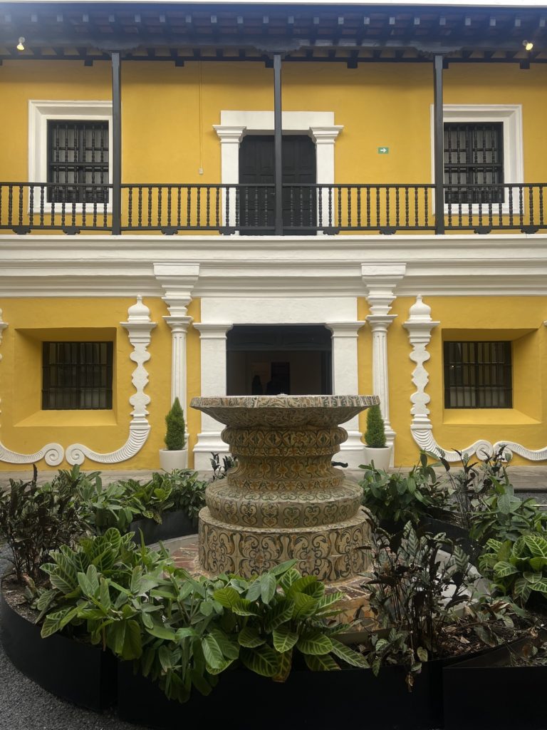 water fountain in the middle of art museum courtyard with yellow building in background