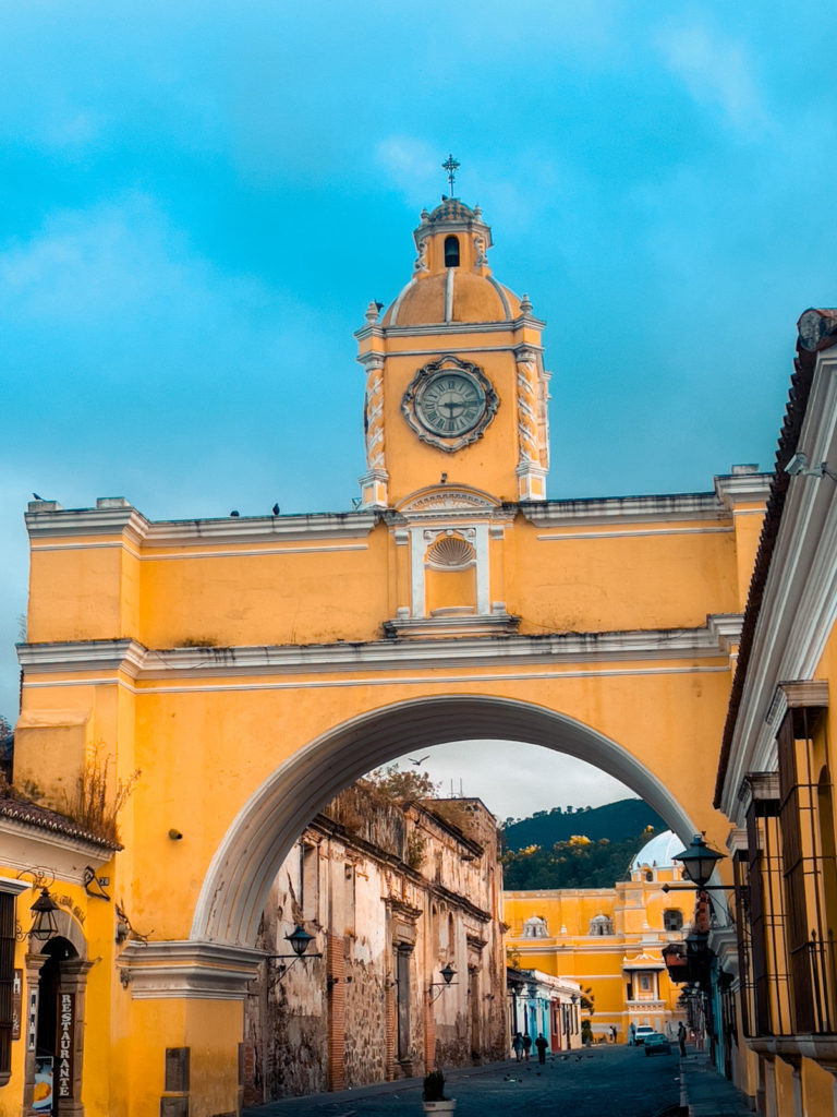 photo of a yellow arch with a tower in the middle and classic antigua cobbled street in the background