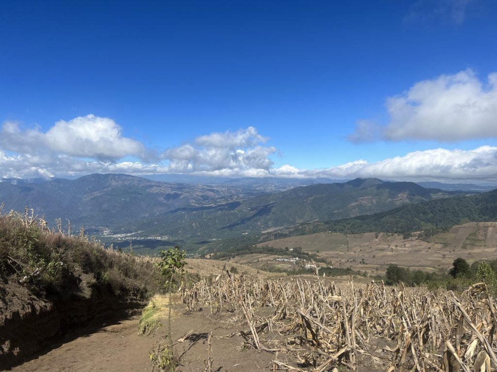 views from the lowest section on the Acatenango hike. with crops on the right, a sandy path on the left and mountainous scenery in the background