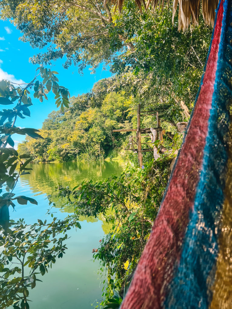 a photo from a hammock with views of a lake shore, with a jumping platform in the background and trees and shrubs surrounding it