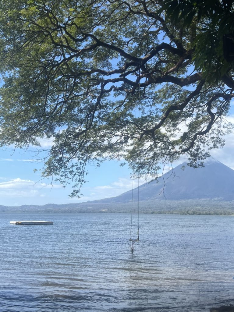photo of lake Nicaragua with swing and platform just a little bit away from shore, with volcano view in the back