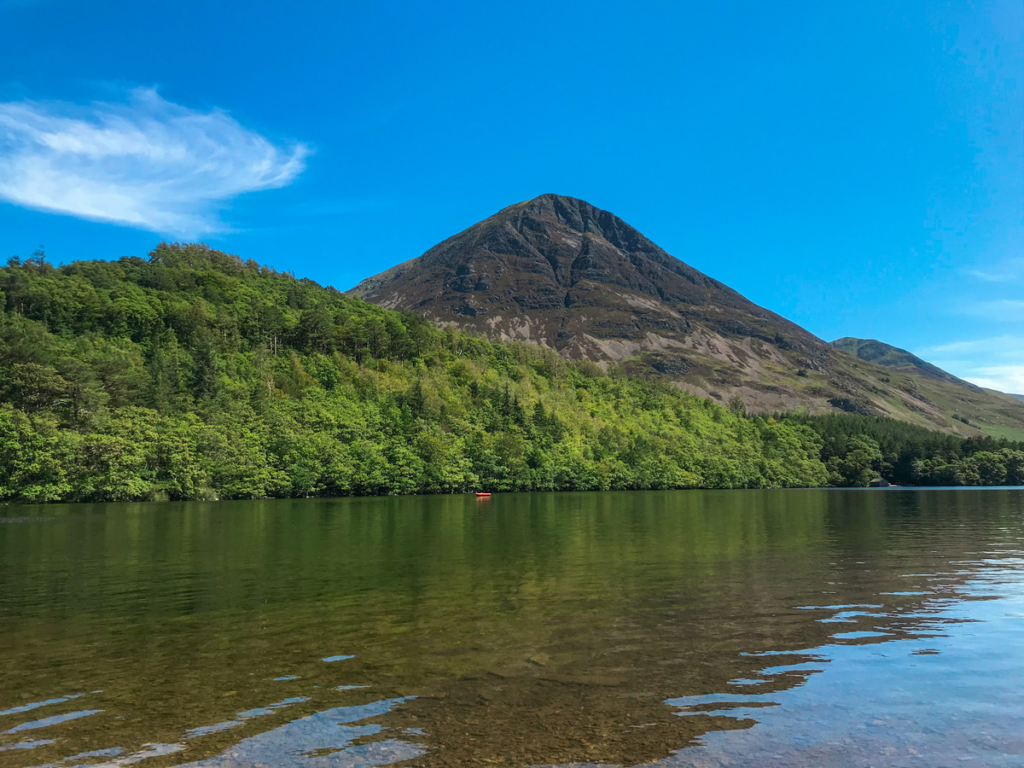 photo of crummock water with kayak, forest and mountain peak in the background