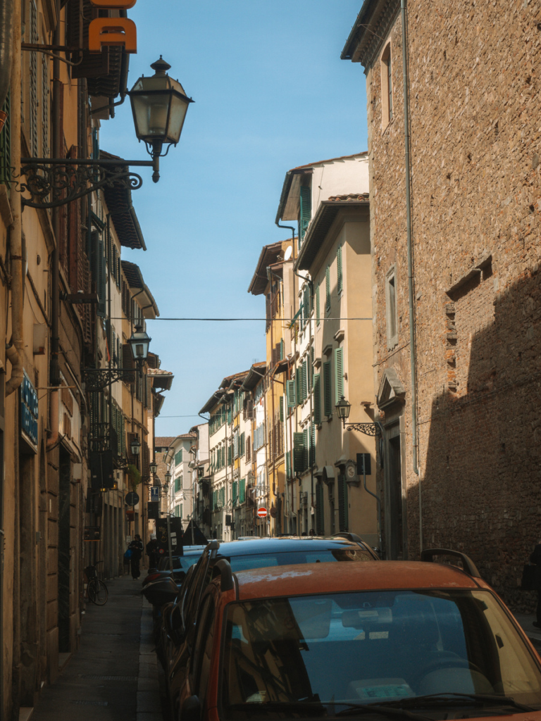 photo of cars along a street in florence with sun shining along the right side of the street